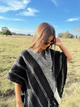 Ruana tejida a mano en telar, confeccionada en lana merino color negro con detalles en blanco y flecos.