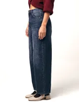 Jean de tiro alto con silueta barrel, caracterizado por su pierna amplia con una leve forma curva. Confeccionado en denim de color azul profundo con un sutil efecto lavado, presenta un diseño de cinco bolsillos y cierre frontal con botón y cremallera.