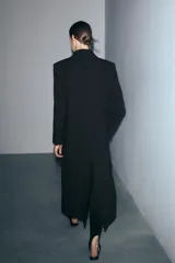Abrigo largo de paño color negro con cuello de solapa, manga larga, cierre frontal con un botón y bolsillos de vivo en el pecho y delantero.