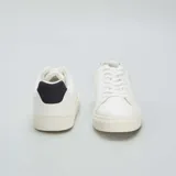 Zapatillas blancas de cuero sintético con cordones, suela plana y detalle de refuerzo negro en el talón.