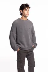 Buzo de punto inglés grueso en color gris melange, de corte amplio con hombros caídos y mangas largas, con sutil bordado de la marca en el pecho.