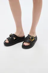 Sandalias negras de plataforma plana, con tiras cruzadas en el empeine con detalles de costuras pespunteadas y una hebilla metálica dorada lateral.