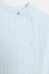 Camisa de corte oversize con estampado de rayas verticales, cuello redondo tipo mao y cierre frontal con botones. Presenta manga larga con puños anchos, un bolsillo de plastrón con solapa en el frente y bajo asimétrico.