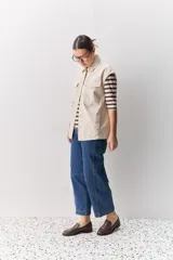 Chaleco de algodón color beige, de calce relajado, con cuello clásico, hombros amplios, cierre frontal con broches metálicos y bolsillos delanteros con solapa.