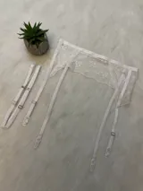 Portaligas de encaje blanco con tiras ajustables y broches metálicos para sujetar medias.