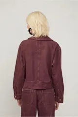 Chaqueta color borgoña de corte recto con cierre frontal metálico y cuello amplio con hebillas decorativas. Cuenta con bolsillos laterales con broches y costuras marcadas que aportan un aire utilitario.