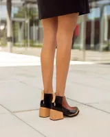 Botinetas de cuero con diseño bicolor, combinando paneles en color negro y marrón con textura de reptil. Presentan un taco cuadrado de madera y suela con plataforma.