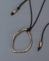 Collar con dije colgante de forma orgánica e irregular, acabado dorado, suspendido de un cordón negro de algodón natural.