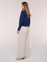 Cardigan corto azul marino de punto, con silueta entallada y largo a la cintura. Cuenta con un ribete decorativo que recorre el cuello redondo y la abertura frontal, integrando una cadena dorada en contraste. Posee bolsillos delanteros simulados y mangas largas.