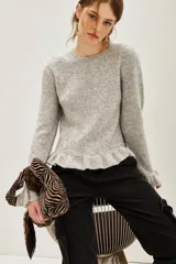 Sweater de punto color gris melange, con cuello redondo, manga larga y detalle de volado en el ruedo. Presenta pequeñas aplicaciones de strass distribuidas por toda la prenda.