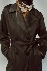 Abrigo largo color marrón oscuro con efecto ante, cuello solapa, manga larga con trabillas en los hombros y bolsillos delanteros de vivo. Presenta un bajo con abertura en la espalda y cierre frontal cruzado con botones, complementado con un cinturón a tono.