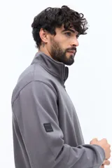 Buzo de algodón color terracota, con cuello alto y cierre parcial frontal. Presenta puños y cintura ajustados, bolsillos laterales y un pequeño logo bordado en el pecho.