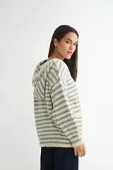 Saco tejido de punto con diseño a rayas horizontales en tonos beige y gris. Presenta capucha con cordones ajustables, cierre frontal con botones de madera, mangas largas y dos bolsillos delanteros.