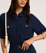 Camisa color fucsia de tejido airflow, con cuello camisero, mangas cortas con pliegues, cierre frontal con botones metalizados y bolsillos con solapa en el pecho.