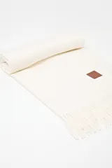 Pashmina de textura suave en color azul, con terminación de flecos en los extremos y un pequeño aplique de cuero sintético con logo grabado.