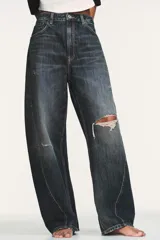 Jeans de tiro medio con diseño baggy balloon, cinco bolsillos y costuras laterales torcidas. Presenta un acabado desgastado con roturas localizadas y cierre frontal con cremallera y botón metálico.