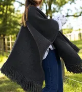 Ruana de lana merino color negro, con diseño tejido en punto arroz y terminación de flecos en todo el borde.