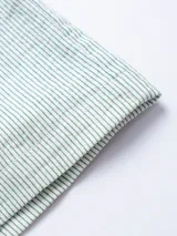 Camisa de manga corta confeccionada en tejido ligero de algodón con diseño de rayas verticales finas. Presenta cuello clásico, cierre frontal con botones de madera, un bolsillo aplicado en el pecho y un pequeño parche decorativo en el ruedo.