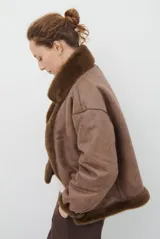 Chaqueta de piel sintética en color burdeos, con cuello alto y cierre frontal oculto. Presenta un diseño de corte recto y mangas largas con puños ligeramente ajustados.
