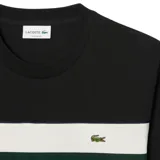 Remera Lacoste negra de manga corta con cuello redondo y franja horizontal blanca y verde en el pecho. Logo de la marca bordado en el pecho.