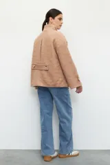 Tapado corto color beige de tejido grueso con cuello alto, cierre frontal con botones grandes veteados y bolsillos delanteros.