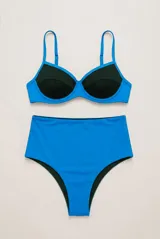Conjunto de bikini bicolor, compuesto por un top con aro y breteles regulables en color azul con detalles negros, y una bombacha tiro alto vedetina en color azul.