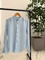 Camisa de lino a rayas celestes y blancas, con cuello mao y botones frontales en tono marrón.
