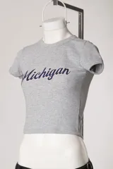 Remera baby tee blanca de morley, con ajuste al cuerpo, mangas cortas, cuello redondo y estampado con la inscripción 'Michigan' en estilo college.