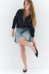 Pollera mini de denim de algodón rígido, color celeste claro con efecto lavado. Diseño acampanado con cintura estándar, cierre frontal con botón y cinco bolsillos.