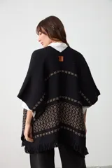 Ruana tejida de corte abierto, color negro con detalles de guardas geométricas en tonos tierra. Presenta terminaciones con flecos en el ruedo.