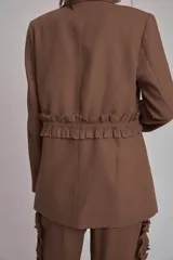 Blazer negro con solapas de muesca, corte holgado, cierre frontal con lazo y detalle de volados en los bolsillos.