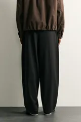 Pantalón de corte balloon fit en color gris oscuro, confeccionado en tejido con viscosa. Presenta pliegues frontales, cintura ajustable con cinturón integrado, bolsillos laterales y bolsillos traseros de doble vivo. Cierre frontal con cremallera y botón.