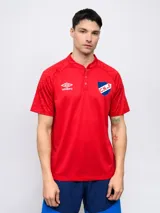 Remera polo de entrenamiento Umbro del Club Nacional de Football, color rojo. Presenta cuello mao con cierre de botones, mangas cortas con textura geométrica sutil, logo de la marca bordado y escudo del club en el pecho.