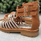 Sandalias bajas de cuero color beige con tiras horizontales plateadas y cierre con hebilla al tobillo.