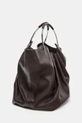 Bolso tipo saca de piel color marrón oscuro, con cuerpo fruncido y doble asa de mano rígida metálica. Incluye asa extraíble para llevar al hombro o cruzado y bolsillo interior extraíble.