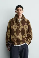 Polo de corte relajado confeccionada en tejido de textura con diseño de rombos en tonos marrones. Presenta cuello de solapa en pana, cierre frontal con botones, mangas largas con puños abotonados y bordado a contraste en el pecho.