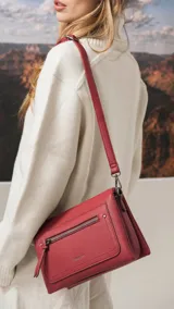 Bandolera de tamaño mediano en color gris, confeccionada en símil cuero con textura granulada. Presenta un bolsillo frontal con cierre, herrajes metálicos oscuros y correa ajustable y desmontable.