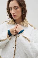 Campera acolchada de corte holgado, color blanco con diseño capitoneado en forma de rombos. Presenta cuello camisero y bordes internos con estampado floral en tonos azul y rojo, cierre frontal con botones a presión y bolsillos laterales.