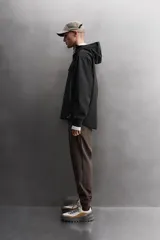 Cazadora deportiva color marrón confeccionada en tejido técnico de tres capas con membrana impermeable. Cuenta con cuello alto con capucha ajustable, mangas largas con puños reforzados ajustables, aberturas con cremallera en axilas, bolsillos frontales con cremallera y bajo ajustable con elásticos laterales.