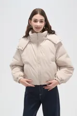 Campera puffer de color beige con cuello alto, capucha desmontable, cierre frontal y bolsillos laterales. Diseño de corte holgado con puños elásticos.