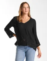 Blusa negra de rayón con caída fluida, escote en V y mangas 3/4 acampanadas. Presenta bordados florales y calados en el ruedo y los puños, con un diseño asimétrico y terminación festoneada.