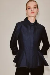 Camisa de denim azul oscuro con cuello solapa, manga larga con puños y diseño peplum en el bajo. Presenta cierre frontal con botones ocultos por solapa.