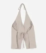 Chaleco color beige con escote halter, corte al cuerpo y cierre frontal con botones. Presenta un bolsillo de ojal en el frente.