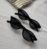 Lentes de sol modelo Soho con armazón ovalado de acetato negro brillante, detalles de tachas metálicas en las esquinas y cristales oscuros con protección UV400.