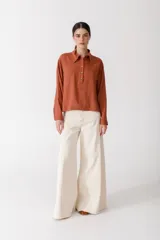 Blusa color ladrillo con rayas verticales finas, cuello polo, mangas largas y cierre parcial con botones.