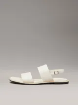 Sandalias planas blancas de cuero sintético, con puntera cuadrada y dos tiras anchas. La tira superior tiene el logo de Calvin Klein grabado.