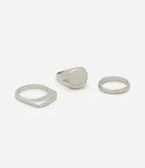 Kit de tres anillos de metal plateado: uno de sello con superficie ovalada, uno con superficie cuadrada y uno de banda simple y fina.