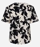 Blusa de manga corta con escote redondo y estampado floral abstracto en blanco y negro. Presenta costuras decorativas en contraste en el cuello y los puños.