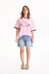 Remera de algodón rosada con diseño oversize y mangas cortas de corte loose fit. Presenta un estampado frontal con la frase "Dolce Vita" y dibujos de fresas, además de ribetes en contraste de tono oscuro en el cuello y los puños.