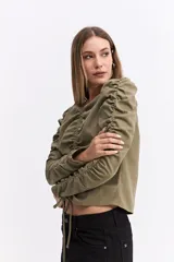 Blusa de manga larga color marrón chocolate, con diseño fruncido central ajustable mediante cordones y mangas con detalle de frunces laterales que aportan volumen.